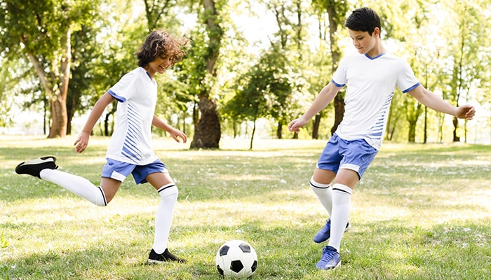 دو نوجوان در حال بازی فوتبال در طبیعت  